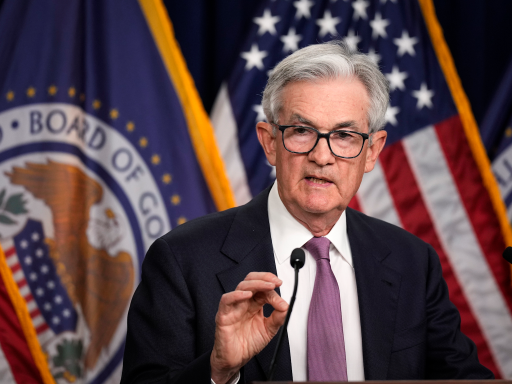 Federal Reserve Chairman Jerome Powell addresses monetary policy with U.S. flags and Federal Reserve emblem in the background 